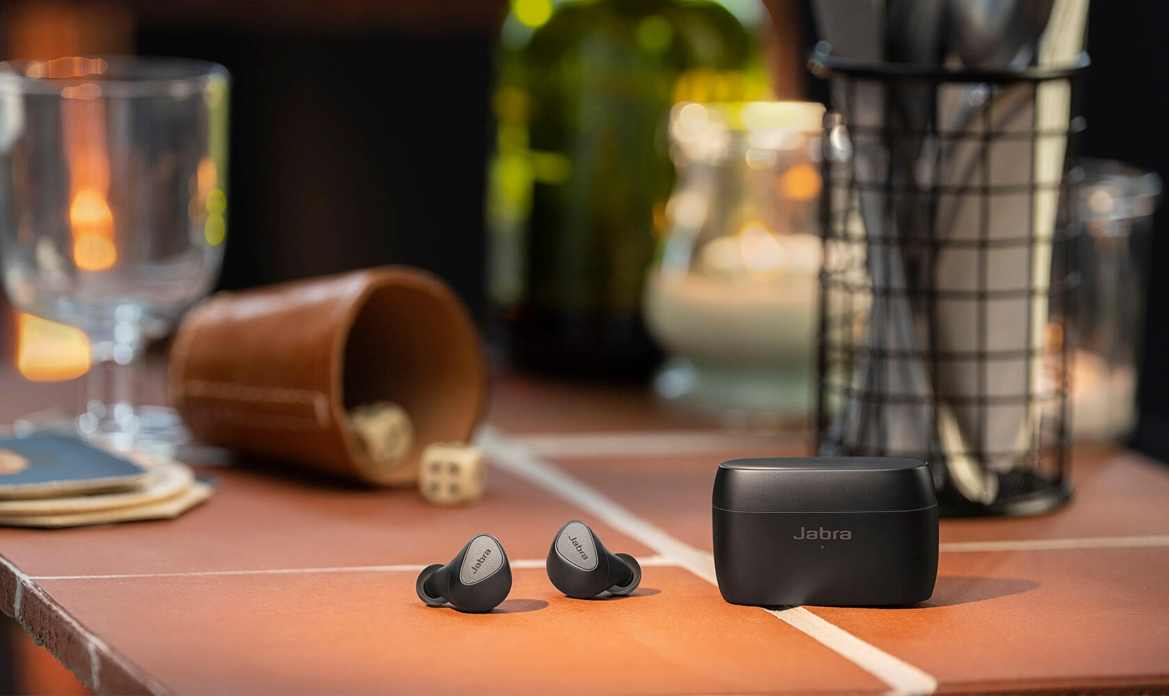 Black Elite 5 earbuds and case in front of a dice game on a bar table